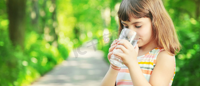 一个孩子在大自然中从玻璃杯里喝水。