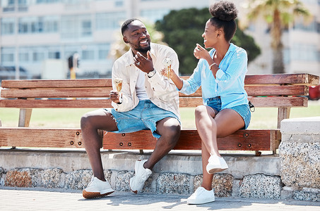 快乐的黑人夫妇一起在沙滩长椅上吃冰淇淋，一边微笑一边大笑。