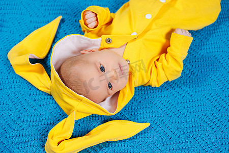 黄色大床摄影照片_一个4-5个月大的小孩穿着黄色衣服躺在床上。