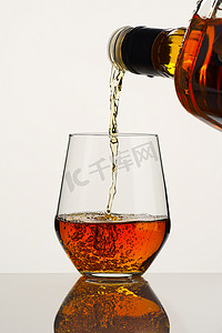 威士忌或白兰地从白色背景的瓶子里倒入玻璃杯中。