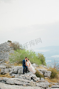 新郎拥抱坐在山顶石头上的新娘