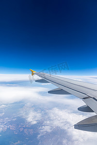 从乘客窗口可以看到蓝天下的飞机机翼在高空云层之上飞行。
