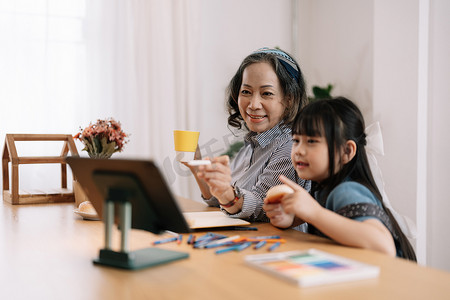 微笑的老奶奶和可爱的小孙女一起在笔记本电脑上看动画片，快乐的老奶奶种植和绘画。