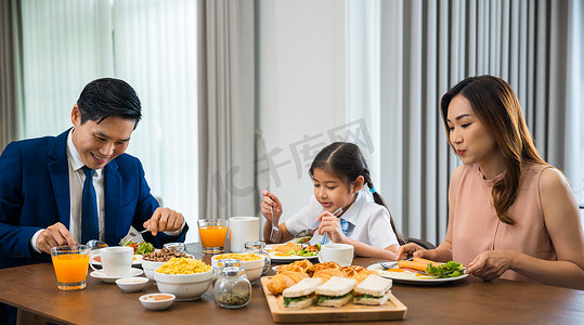 早上喝牛奶摄影照片_亚洲家庭早上在家一起在餐桌厨房吃健康早餐
