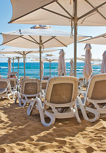 夏季，金色沙滩上一排排塑料躺椅/休闲躺椅/日光浴床，配有遮阳伞