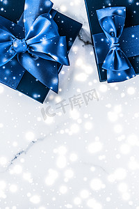 时尚礼盒摄影照片_冬季节日礼盒，配有蓝色丝绸蝴蝶结、大理石背景上的雪花，作为豪华美容品牌的圣诞和新年礼物，平铺设计