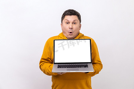 电脑操作系统摄影照片_男子拿着白色笔记本电脑，张开嘴看着相机，对操作系统感到震惊。