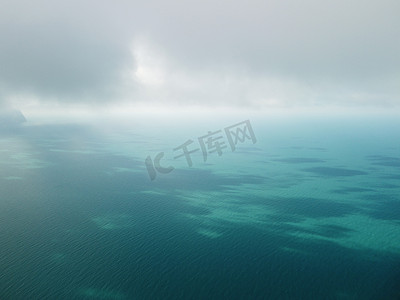 海洋模糊摄影照片_从空中俯瞰平静的蔚蓝大海和火山岩石海岸。