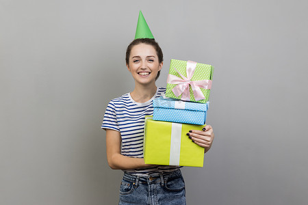 戴着派对锥的微笑的女人，拿着一堆礼物盒，庆祝生日。