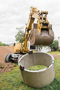带铲斗的液压活塞系统挖掘机，在钢缆混凝土下水道环上提升。