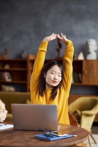 在家或咖啡馆用笔记本电脑工作的亚洲女性疲惫地伸展身体