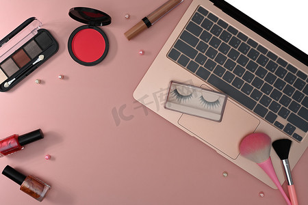 顶视图女性工作区配有笔记本电脑、化妆刷和粉红色背景的化妆品。