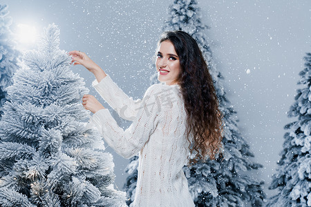 新年前，穿着温暖的白色毛衣和白色袜子的漂亮女孩靠近雪树。