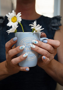 一位年轻女子拿着一杯蓝色的雏菊，这是美丽的夏日美甲