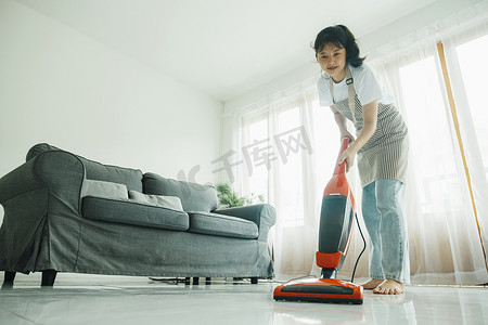 打扫房子摄影照片_年轻女子用吸尘器打扫房子。