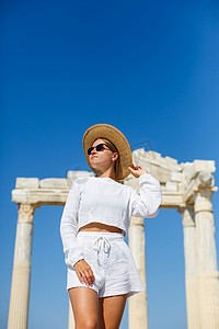 一位年轻苗条的晒黑女人，穿着白色短裤和T恤，戴着墨镜和帽子。