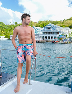 蜜月假期摄影照片_穿着泳裤的年轻男子乘船游览圣卢西亚，豪华假期圣卢西亚加勒比海