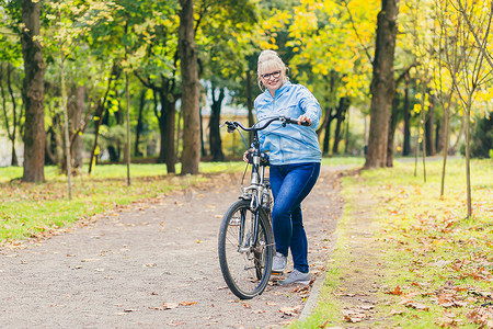 公共自行车摄影照片_金发美女在公园、树林、大自然中骑自行车，听音乐，积极花时间，做运动，快乐