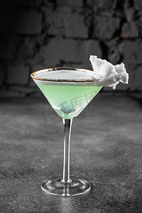 绿色酒精鸡尾酒在玻璃杯中装饰着灰色背景的棉花糖。
