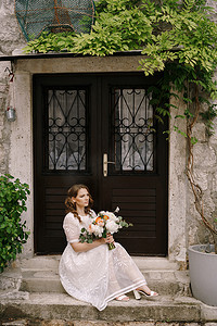 有花束的新娘坐在老房子门前的台阶上