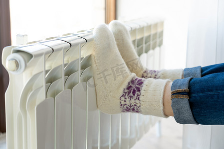 穿着羊毛袜在加热器上用脚取暖的妇女