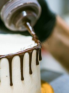 融化的巧克力滴摄影照片_蛋糕设计师用巧克力甘纳许滴釉，奶油白色光滑蛋糕