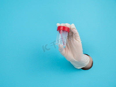 一名戴着橡胶手套的妇女的手从蓝色的纸背景中伸出，手里拿着一个收集粪便的容器。