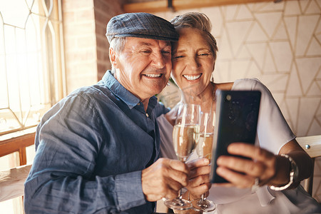 老夫妇在家里用手机、香槟和爱情自拍，庆祝结婚纪念日、庆祝活动或生日。