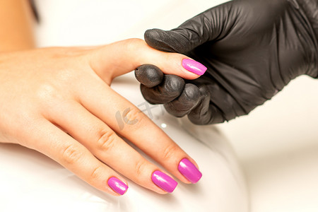一位美甲师在美甲沙龙里握着美丽的年轻女手，展示着完成的紫色、粉色指甲油。