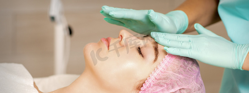 这名妇女正在美容院接受美容治疗，戴着医用手套的美容师正在水疗沙龙触摸女性的脸部。