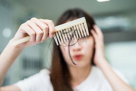 亚洲女性有长脱发问题，头发附着在梳子上。