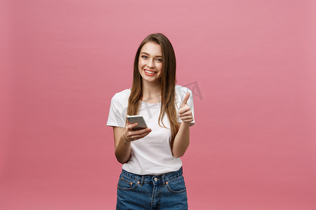 照片中，快乐可爱的美丽年轻女子在粉红色的墙壁背景下用手机聊天。