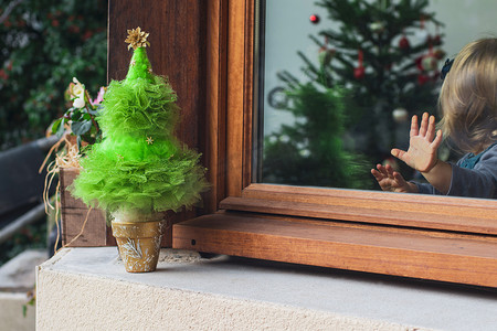 圣诞舞会摄影照片_手掌放在玻璃上看着树的小女孩