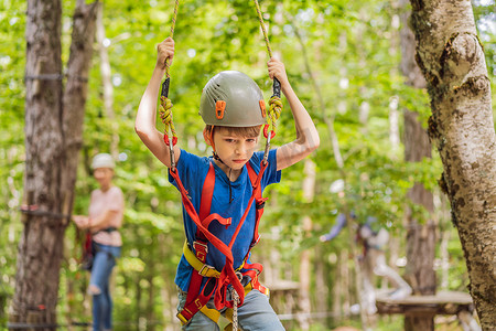 滑索摄影照片_母亲和儿子在森林里的极限公路电车滑索上攀登树上的登山绳安全连接到树顶绳索冒险公园。