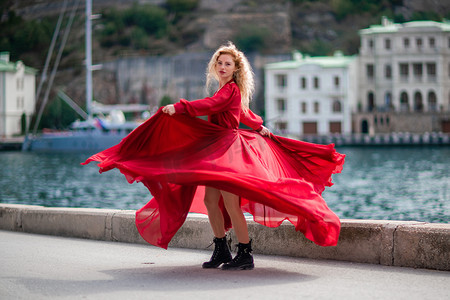 一个穿着红色连衣裙的女人，一个穿着飘逸连衣裙、长着长丝翅膀的时装模特，堤岸上飞扬着织物。