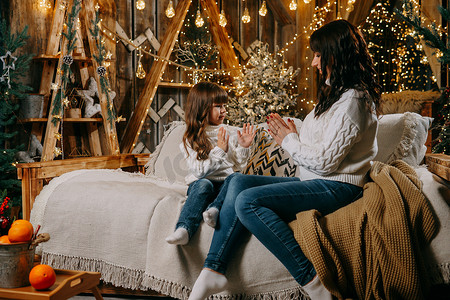 一个小女孩和她的母亲在圣诞树旁边的沙发上享受舒适的家庭环境。