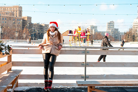 美丽可爱的年轻成年女性深色头发温暖的冬季夹克站在溜冰场背景城镇广场附近。