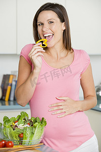 孕妇在厨房里做沙拉，微笑着