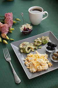 牛油果咖啡摄影照片_每人营养早餐：炒鸡蛋、橄榄、橄榄、牛油果、奶酪和覆盆子果酱。