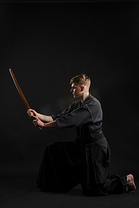 穿着传统日本和服的剑道大师正在黑色工作室背景下用竹剑练习武术。