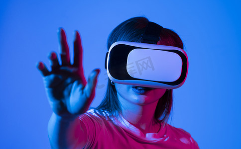 身穿白色 T 恤、兴奋的黑发女性使用虚拟现实 VR 耳机眼镜获得经验，在霓虹灯下双手打手势。