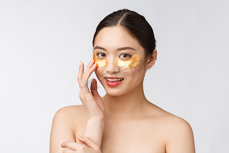 面部护理少女摄影照片_亚洲美女少女用眼下的金色眼罩贴片护理皮肤