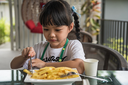年轻的亚洲女孩吃炸薯条小孩有趣快乐的土豆快餐。