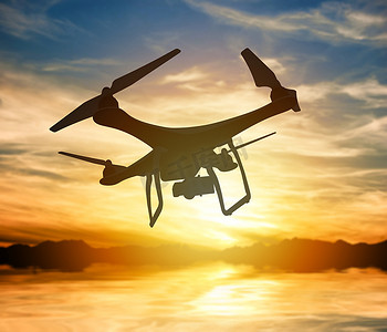 无人机剪影摄影照片_一架带有数码相机的无人机在夕阳天空中飞行的剪影