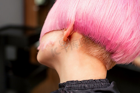 在美发沙龙里为年轻模特的后视图设计和剪裁染成粉红色的头发。