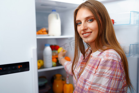 冰箱里摄影照片_一位年轻金发女子从冰箱里拿食物的肖像