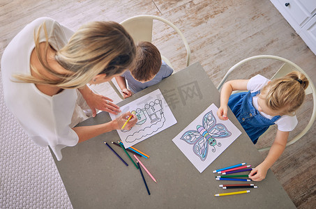 上面的照片是小女孩和男孩坐在桌边，拿着彩色铅笔和图片，在妈妈的帮助下着色。