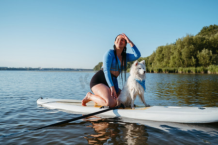 清晨，快乐的年轻女子和她的狗日本狐狸坐在 Sup 板上享受湖边的生活