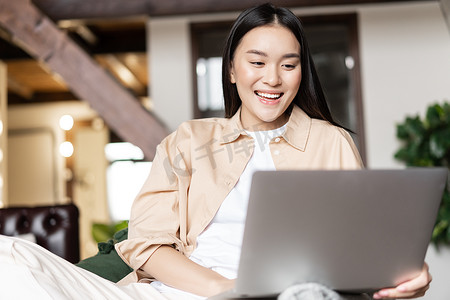 快乐的亚洲女性在家休息，用笔记本电脑观看视频或在电脑上浏览网站