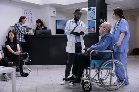老年残疾男子得到护理护士的帮助，与拿着剪贴板的医生交谈